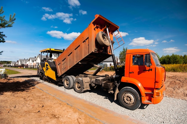 Foto un camión volquete descarga asfalto caliente en una extendedora de asfalto para la construcción de una nueva carretera en el verano en una nueva aldea