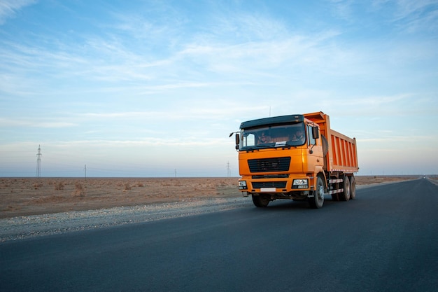 Un camión volquete naranja en una carretera del desierto contra un hermoso fondo de cielo