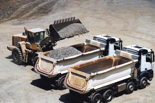 Camiones volquete que se cargan en trabajos de mina de mineral en la mina a cielo abierto Cargadora de ruedas cargando camiones volquete