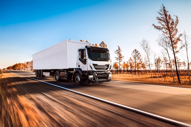 Camioneta blanca con remolque blanco en la carretera en otoño