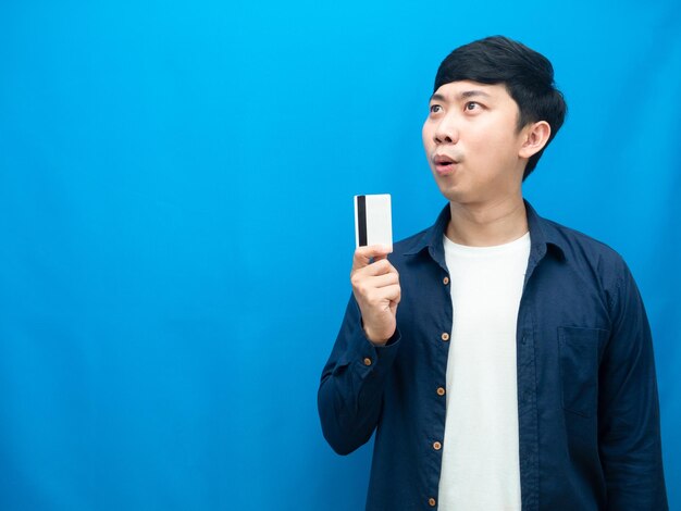 Camisa azul de homem mostrando cartão de crédito se sente animado olhando para o fundo azul do espaço de cópia