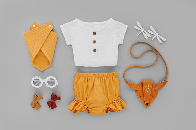 Camisa blanca, pantalón corto naranja con bolso infantil y gafas de sol. Conjunto de ropa de bebé y accesorios para vacaciones de verano sobre fondo gris. Traje de moda infantil. Endecha plana, vista superior