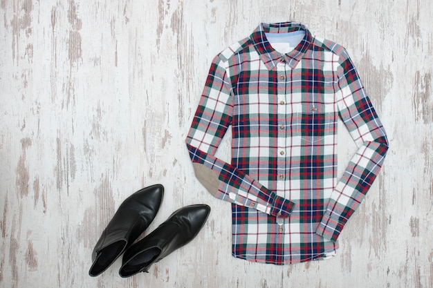 Camisa a cuadros y zapatos negros sobre superficie de madera