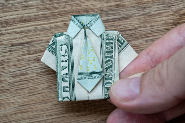 Camisa de origami feita de notas de dólar e mão em fundo de madeira Camiseta Nota de dólar fechada