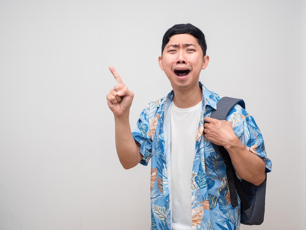 Camisa de praia de homem positivo com mochila aprecia feliz com o dedo de ponto de gesto de férias isolado