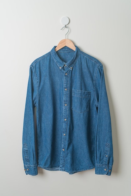 Foto camisa jeans pendurada com cabide de madeira na parede