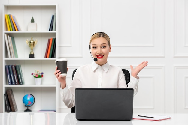 Camisa de oficina de linda chica rubia de servicio al cliente con auriculares y computadora agitando las manos y sonriendo