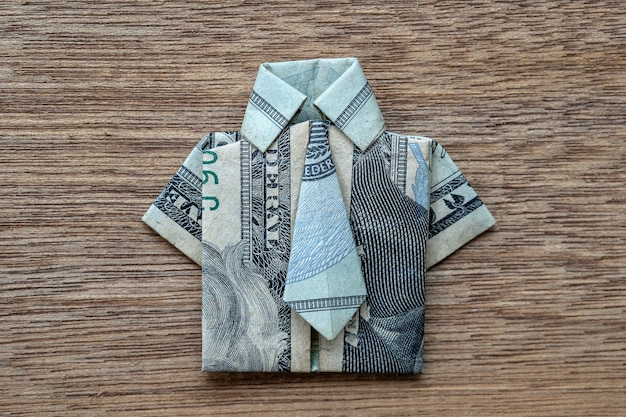 Camisa de origami hecha de billetes de dólar sobre fondo de madera. De cerca. Camiseta con diseño de billete de dólar