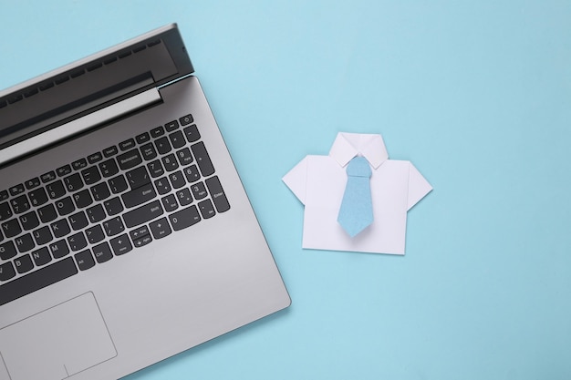 Camisa de papel de origami con corbata y computadora portátil sobre fondo azul Concepto de negocio trabajo en línea