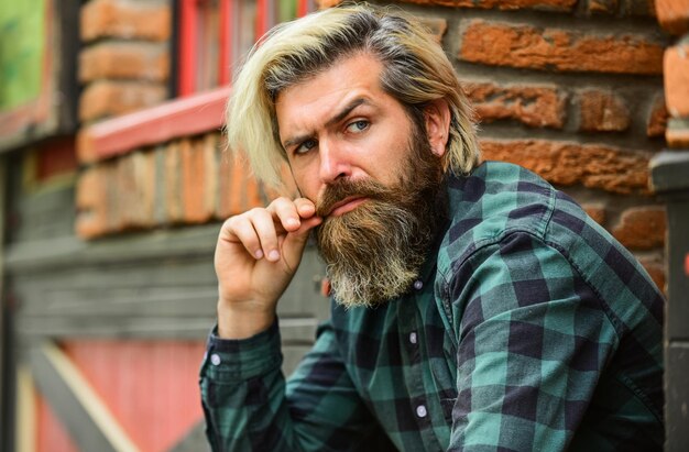 Camisa quadriculada de homem barbudo deprimido hipster cabelo tingido e barba homem moda casual hipster em óculos de sol cabeleireiro e barbearia macho brutal com cabelo loiro fundo de arquitetura irlandesa