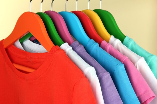 Camisas diferentes en perchas de colores sobre fondo beige