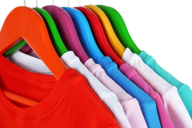 Foto camisas diferentes en perchas de colores sobre fondo blanco.