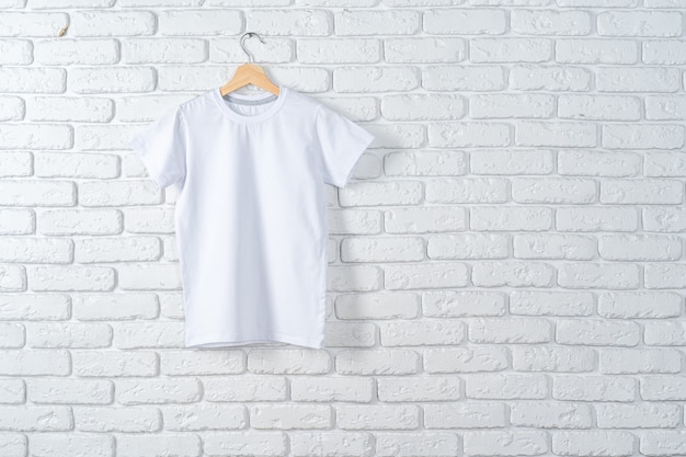 Camiseta blanca colgada en la percha contra la pared de ladrillo, espacio de copia