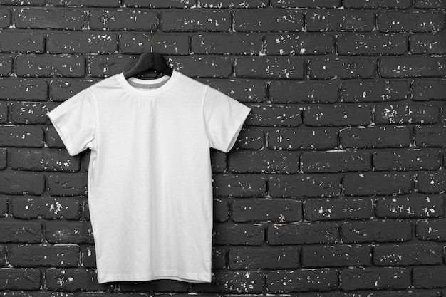 Camiseta blanca colgada en la percha contra la pared de ladrillo, espacio de copia