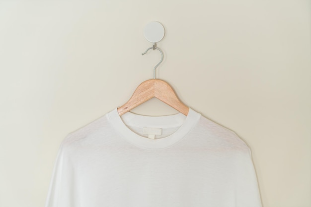 camiseta blanca colgada con percha de madera en la pared