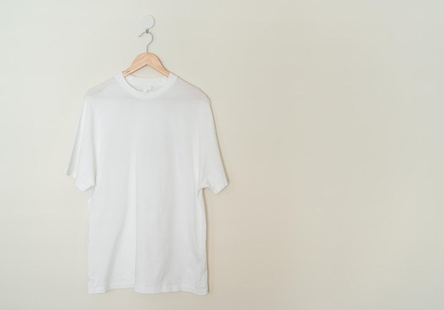 camiseta blanca colgada con percha de madera en la pared