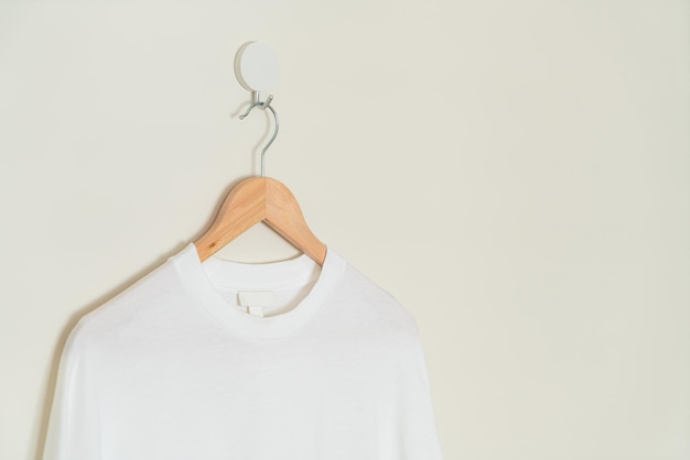 Foto camiseta blanca colgada con percha de madera en la pared