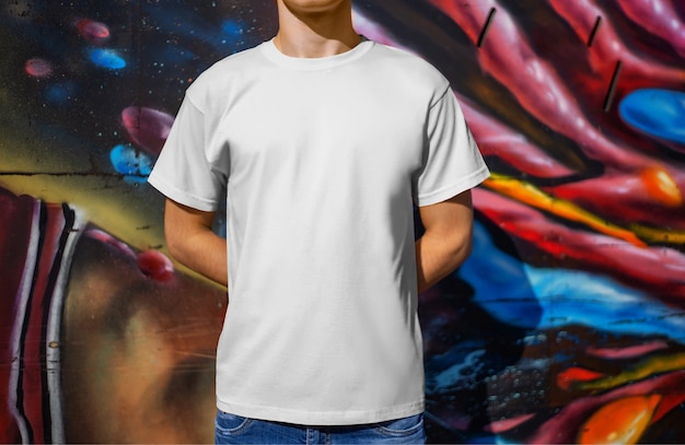 Camiseta blanca de maqueta de un chico joven, contra el fondo de una pared con graffiti, vista frontal. Ropa para publicidad en la tienda. Plantilla para la presentación de su diseño y patrón.