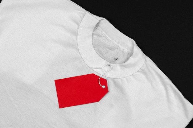 Camiseta blanca sobre un fondo negro con una etiqueta roja en blanco Etiqueta de precio roja vacía en una camiseta blanca