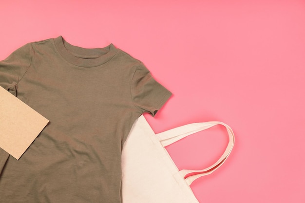 Camiseta en blanco, bolsa y hoja de cartón sobre fondo rosa