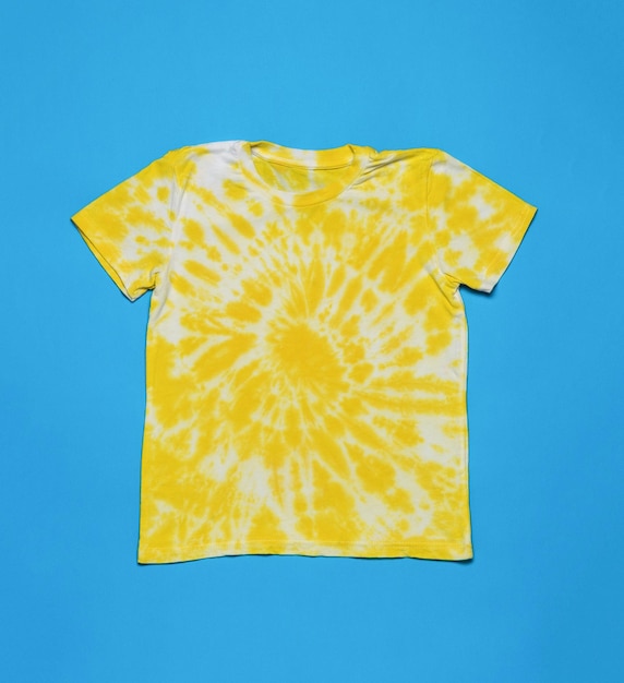 Camiseta branca e amarela pintada em um estilo de tintura de gravata espiral em um fundo azul postura plana