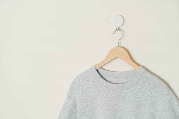 Foto camiseta gris colgada con colgador de madera en la pared