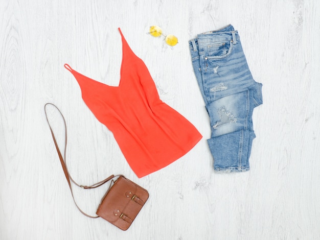 Foto camiseta sin mangas naranja, jeans rotos, bolso y gafas de sol. concepto de moda