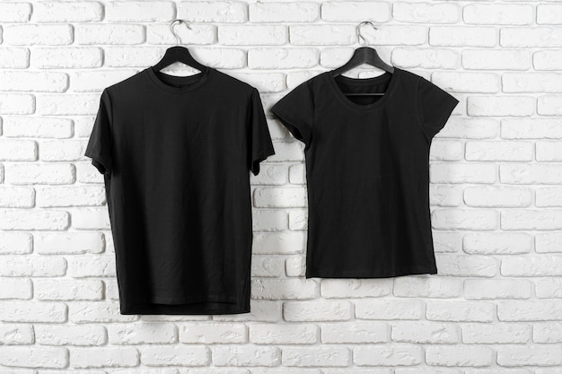 Camiseta negra colgada en una percha contra la pared de ladrillo, vista frontal