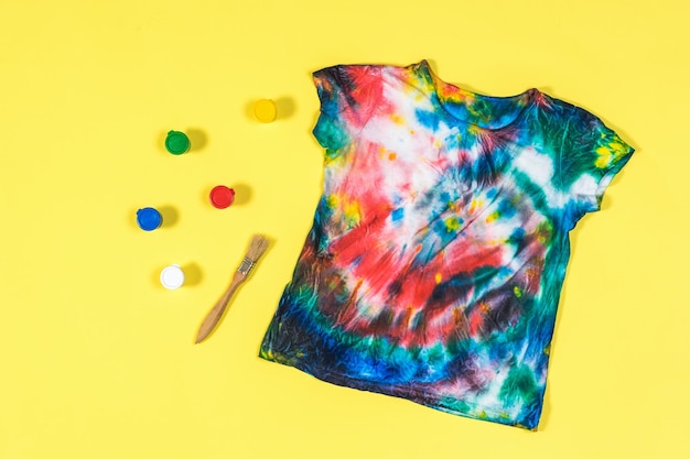 Camiseta tie dye com cores espalhadas em um fundo amarelo postura plana