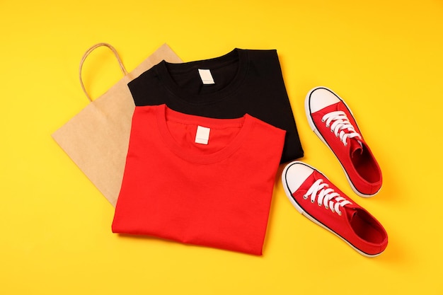 Camisetas en blanco, zapatillas y bolso sobre fondo amarillo.