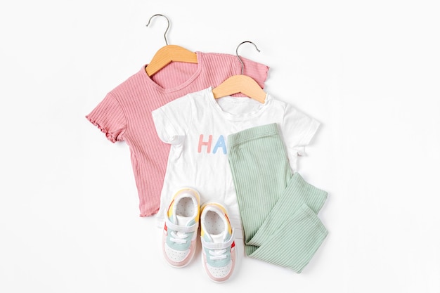 Camisetas colgadas y zapatillas deportivas. Conjunto de ropa de bebé y complementos para primavera, otoño o verano sobre fondo blanco. Traje de moda para niños. Endecha plana, vista superior