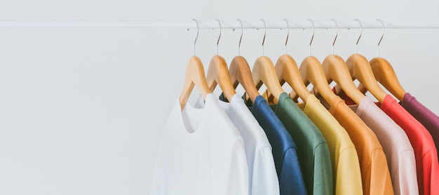 Camisetas coloridas en una percha de madera colgada en un perchero sobre fondo blanco