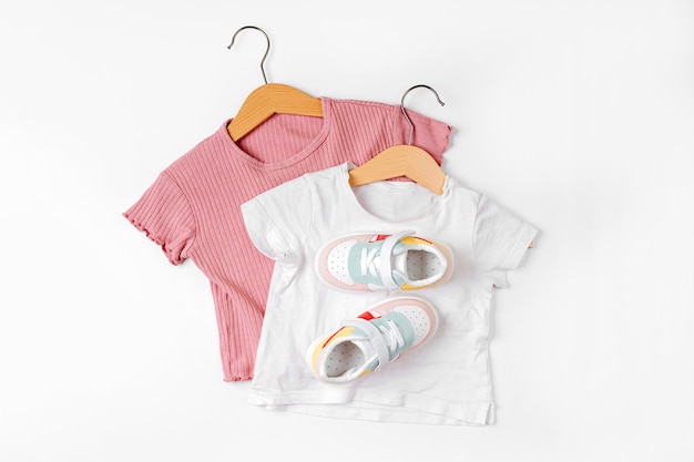 Foto camisetas em cabide e tênis. conjunto de roupas de bebê e acessórios para a primavera, outono ou verão em fundo branco. roupa de moda infantil. camada plana, vista superior