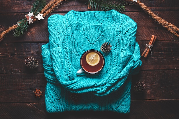 Camisola quente, pinhas, uma caneca de chá quente com limão, canela e anis estrelado. Roupas de inverno e bebidas. Conceito de inverno.