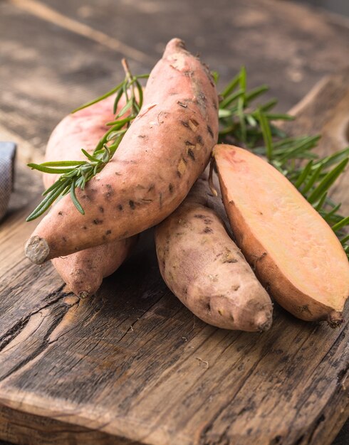 Camote en el fondo de la tabla de madera, de cerca. Batatas crudas o batatas con hierbas