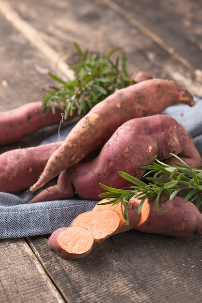 Camote en el fondo de la tabla de madera, de cerca. Batatas crudas o batatas con hierbas