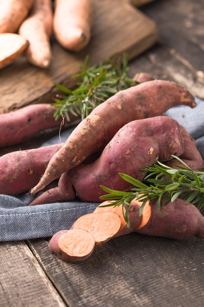 Camote en el fondo de la tabla de madera, de cerca. Batatas crudas o batatas con hierbas