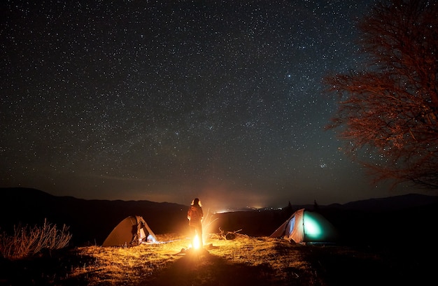 Campamento nocturno. Caminante descansando junto a la fogata bajo el cielo estrellado