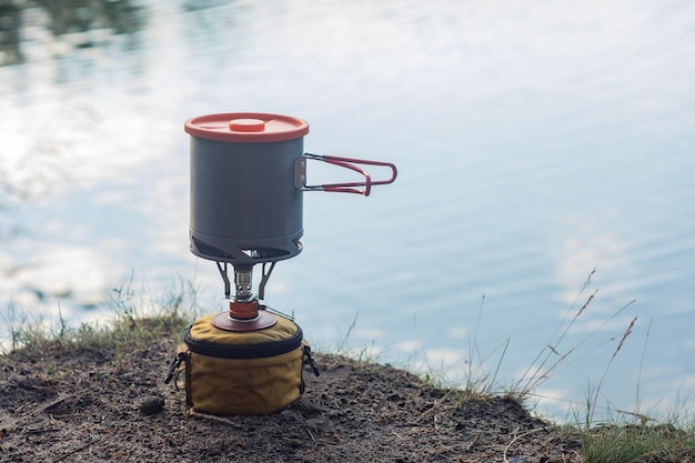 Campamento de verano al aire libre contra el fondo del lago Quemador de gas turístico con sartenes para cocinar