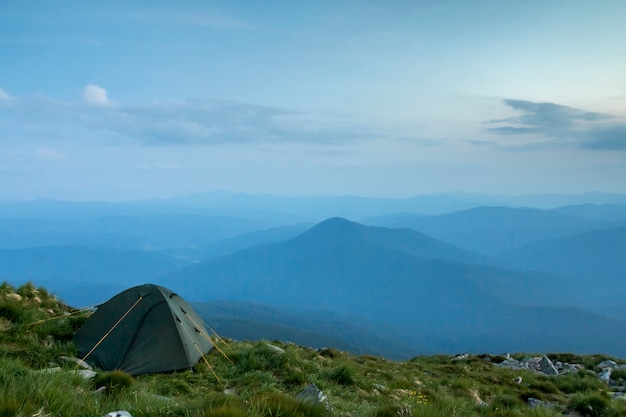 Campamento de verano en las montañas al amanecer. Tienda turística en la colina cubierta de hierba redonda en las distantes montañas de niebla azul rango bajo el cielo rosado antes del amanecer o atardecer. Concepto de turismo, senderismo y belleza de la naturaleza.