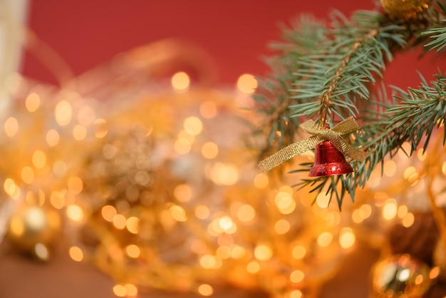 Campana de juguete de Navidad dorada en una rama de abeto en el fondo de una guirnalda de Navidad