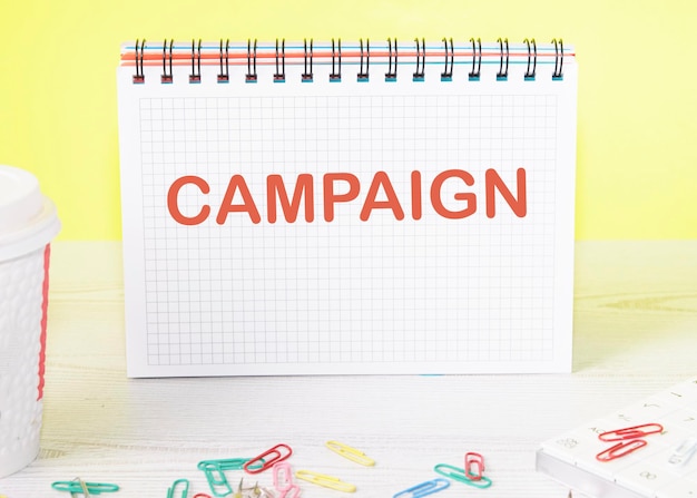 Foto campaña la palabra está escrita en una hoja en blanco en un cuaderno sobre una mesa sobre un fondo amarillo