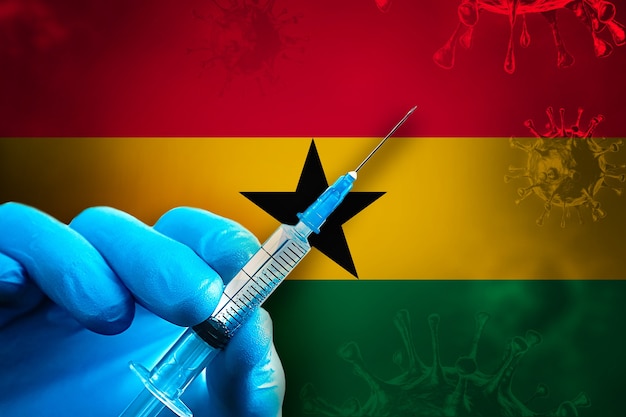 Campaña de vacunación Covid19 de Ghana La mano en un guante de goma azul sostiene la jeringa frente a la bandera