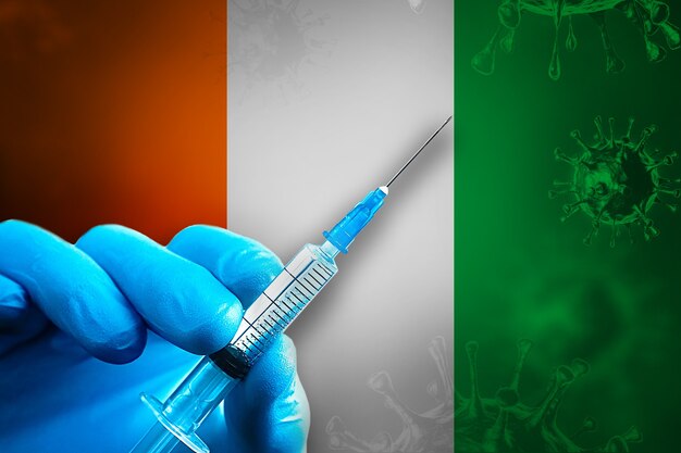 Campaña de vacunación IvoryCoast Covid19 Mano en guante de goma azul sostiene la jeringa frente a la bandera