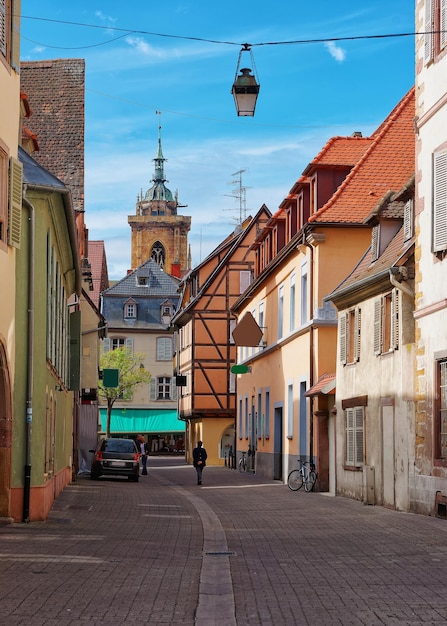 Campanario de la Catedral de San Martín y calle estrecha en el centro de la ciudad vieja de Colmar, Haut Rhin en Alsacia, Francia. gente en el fondo