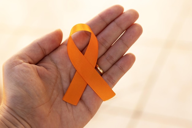 Foto campanha de conscientização da esclerose múltipla em agosto laranja mão segurando a fita laranja
