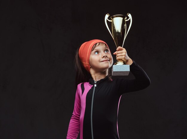 Campeão de menina skatista feliz detém a taça do vencedor. Isolado em um plano de fundo texturizado escuro.