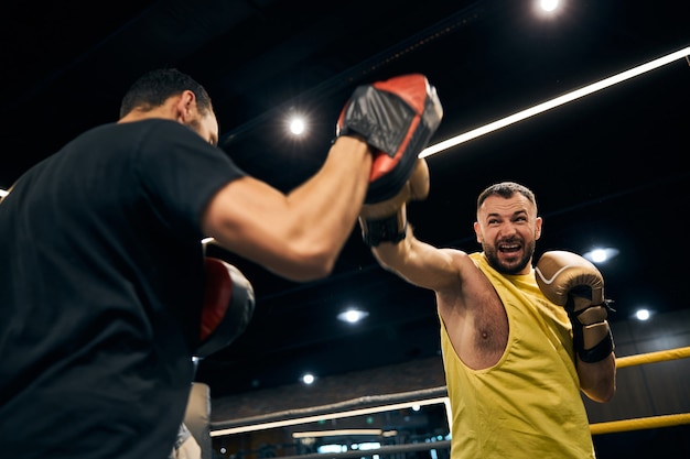 Campeão furioso atacando um painel de foco de boxe na mão de seu treinador