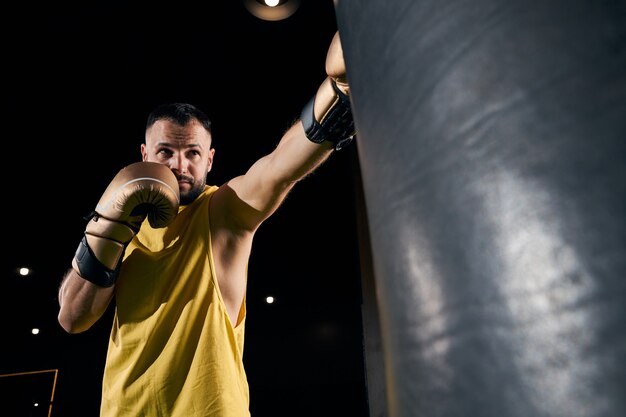 Foto campeão vestindo uma camisa sem mangas dando um golpe certeiro em um saco de areia de boxe