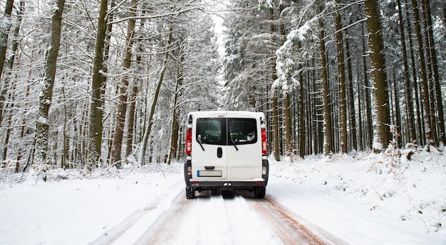 Camper Van dirigindo em uma estrada através de uma floresta coberta de neve no inverno, férias de aventura